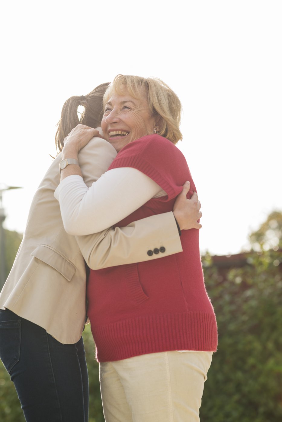Older woman laughing as she hugs a younger woman outdoors